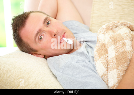 Man with cold laying on sofa with thermometer in mouth Stock Photo