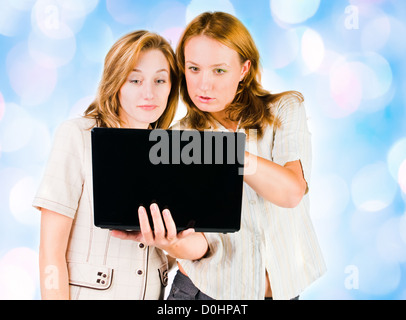 Two young businesswomen working on laptop with blue lights in the background . Stock Photo