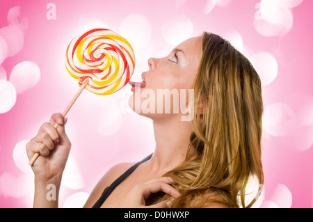 Woman licking sweet sugar candy closeup with pink lights in the background Stock Photo
