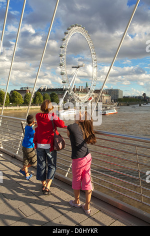 A mother and her children enjoy the view of the London Eye from the Hungerford Bridge over the river Thames. Stock Photo