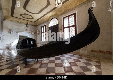 An antique gondola painted black, with a covered cabin, on display at the C'a Rezzonico museum in Venice