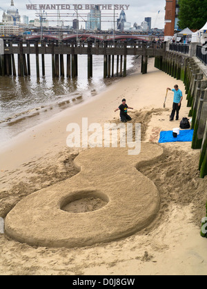 People building a giant guitar sand castle at low tide as part of the Thames Festival. Stock Photo