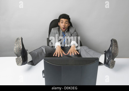 Businessman looking surprised with his feet up in front of a desktop PC Stock Photo