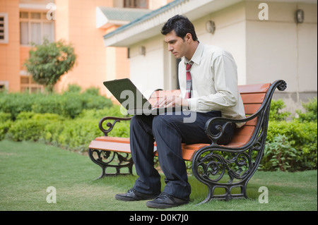 Businessman sitting on the bench and using a laptop Stock Photo