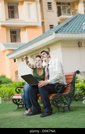 Couple sitting on the bench with laptop and pointing Stock Photo