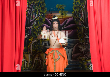 Stage artist dressed-up as Rama blessing and holding a conch shell Stock Photo