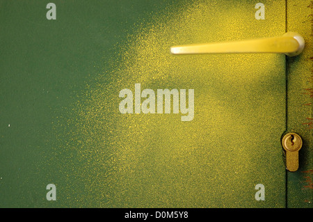 Yellow paint sprayed over green metal door and handle. Abstract background. Stock Photo