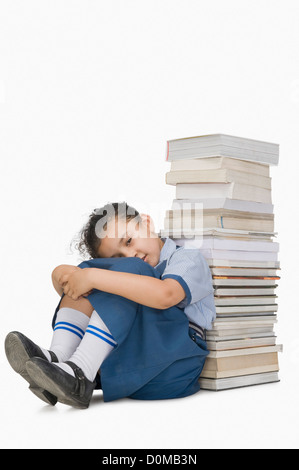 Schoolgirl leaning against a stack of books and looking sad Stock Photo
