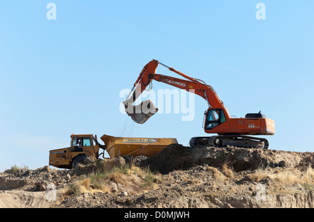 Daewoo excavator working in a construction site loading an articulated Volvo dumper truck Stock Photo