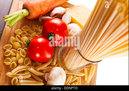 Different types of pasta and vegetables on wooden board