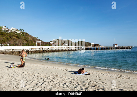 cruise ship dock pier & uncrowded beach with bright sun blue sky at deep water port bahia de Santa Cruz Huatulco Mexico Stock Photo