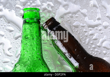 Closeup of two beer bottles on a wet stainless steel surface. One bottle is green the other brown.