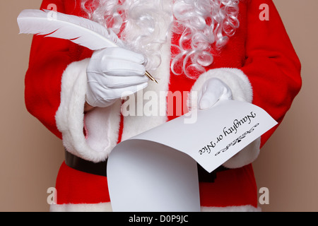 Santa Claus holding a quill pen whilst checking the naughty or nice list. Stock Photo