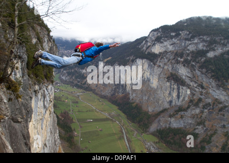 BASE jumper is exiting from a cliff down into the deep valley. Thereby he's keeping his arms up to be stable and be save. Stock Photo