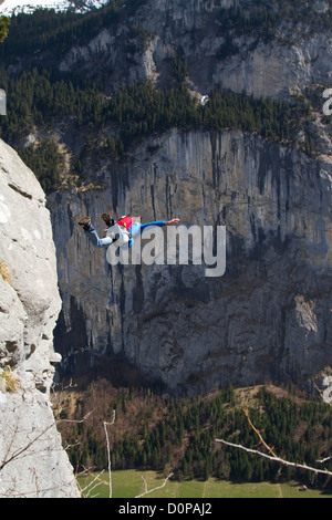 BASE jumper is exiting from a cliff down into the deep valley. Thereby he's keeping his arms up to be stable and be save. Stock Photo