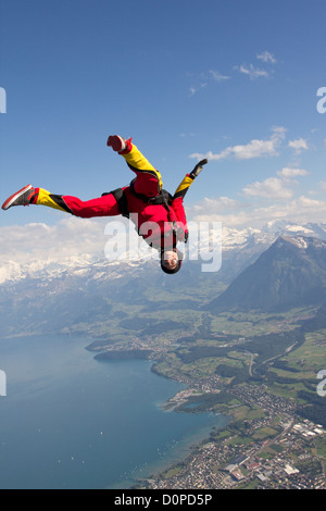 Skydiver girl is flying head low over a beautiful lake. She tries to do a free style position with high speed of 125mph. Stock Photo