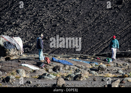 MOUNT KILIMANJARO, Tanzania — Two porters lay out their clothes and sleeping bags at Moir Hut Camp to try to dry them in the sunlight before they have to head off for that day's climb on Mt Kilimanjaro's Lemosho Route. Stock Photo