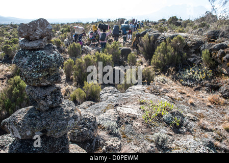 MT KILIMANJARO, Tanzania - A stone cairn next to the path of the Lemosho Route on Mt Kilimanjaro as a group of porters walk by. Stock Photo
