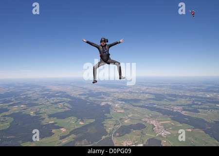 Fun diver is free falling through the blue sky in a sit position and waiting for his colleagues to play with them. Stock Photo
