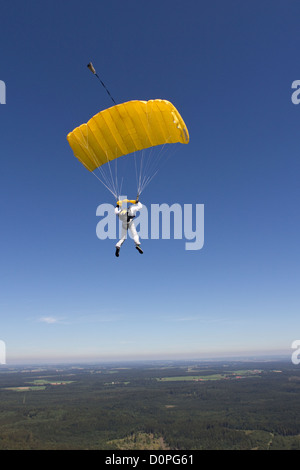 Skydiver under canopy in the blue sky is flying over big forest and is looking out for a suitable landing area. Stock Photo