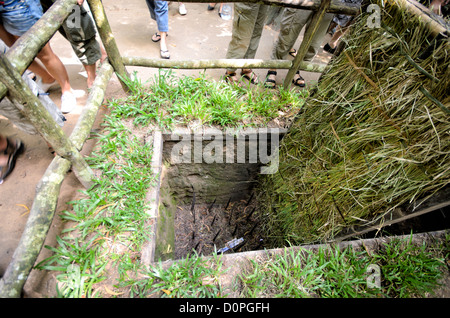 HO CHI MINH CITY, Vietnam — A tour guide demonstrates a preserved punji trap at the Cu Chi Tunnels historical site, showing visitors one of many defensive measures used during the Vietnam War. The camouflaged trap features a concealed pit with metal spikes, a common defensive technique employed throughout the conflict. The demonstration is part of the site's educational exhibits showcasing Vietnamese military tactics. Stock Photo