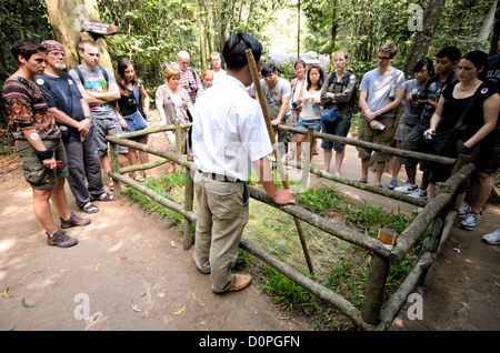 HO CHI MINH CITY, Vietnam - A tour guide demonstrates how one of the many booby traps that were used in the area worked. Inside the fenced area, the grass camouglages a trapdoor that swings down to reveal metal spikes at the bottom of a pit. The Cu Chi tunnels, northwest of Ho Chi Minh City, were part of a much larger underground tunnel network used by the Viet Cong in the Vietnam War. Part of the original tunnel system has been preserved as a tourist attraction where visitors can go down into the narrow tunnels and see exhibits on the defense precautions and daily life of the Vietnamese who l Stock Photo