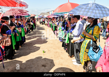 Hmong New Year Ball Game Traditional Costumes Umbrellas Phonsavan Laos // PHONSAVAN, Laos — Young Hmong men and women stand in parallel lines to play *pov pob*, a traditional ball-tossing game held during the post-harvest New Year festival. The rhythmic exchange of a small ball serves as a formalized courtship ritual. Because strict Hmong customs dictate exogamy — requiring marriage outside one's own clan — this annual gathering historically provided a crucial, socially sanctioned venue for teenagers from dispersed villages to find eligible spouses. Stock Photo