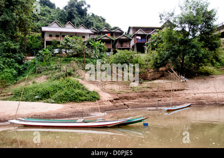 NONG KHIAW, Laos - Boats and hotel rooms on the banks of the Nam Ou (River Ou) in Nong Khiaw in northern Laos. The small farm area will be covered with water when the river rises in the rainy season. At top right you can see a small section of the high bridge crossing the river. Stock Photo