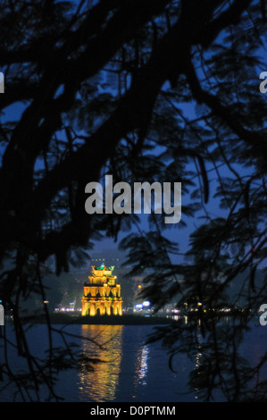 Turtle Tower (also known as Tortoise Tower on a small island in Hoan Kiem Lake in the historical center of Hanoi, Vietnam. The lights of the tower are on and reflected on the water, with the image framed by the branches of a tree on the shore. Stock Photo