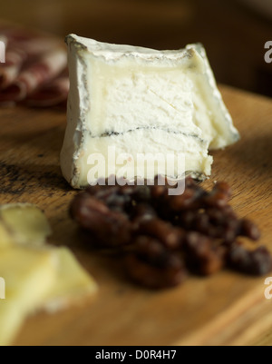 Close up of fine cheese with small fruits in foreground and fine ham in the background. Stock Photo