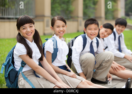 Lively schoolchildren in uniform sitting on floor at school yard Stock Photo
