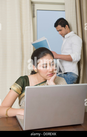 Woman working on a laptop while her husband reading newspaper Stock Photo