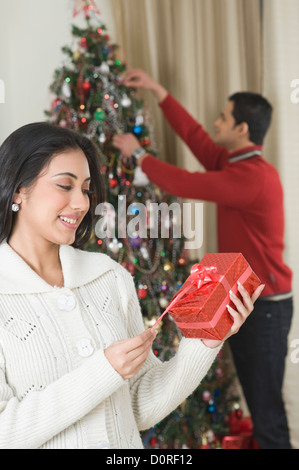 Woman holding a present while her husband decorating Christmas tree Stock Photo