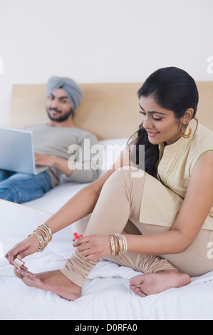 Woman painting toenails while her husband working on a laptop Stock Photo