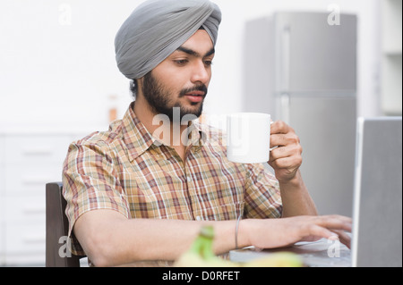 Man working on a laptop while drinking tea Stock Photo