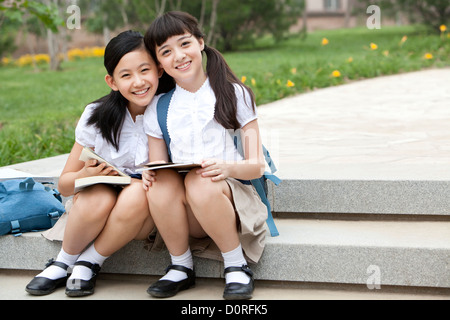 Schoolgirls sitting on steps with books smiling happily outside Stock Photo