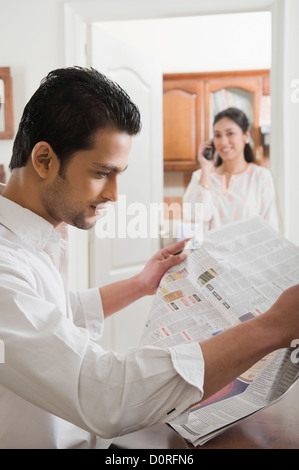 Man reading a newspaper while his wife using a mobile phone Stock Photo
