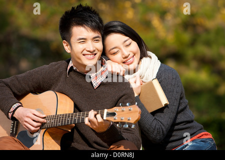 Sweet college couple with guitar and books enjoying the sunny autumn on campus Stock Photo