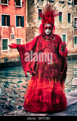 Masked participant posing along a canal on Burano Island during Carnival in Venice, Italy Stock Photo