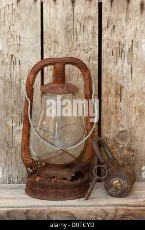 Rusted kerosene lantern with pirate barrel lock and key on old weathered wood shelf Stock Photo