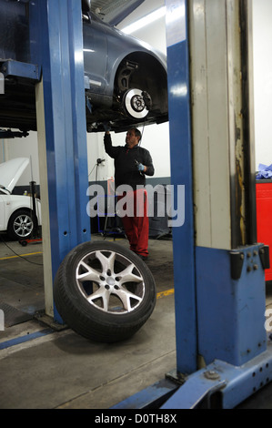 Car mechanic checking a car raised on a hydraulic lift Stock Photo