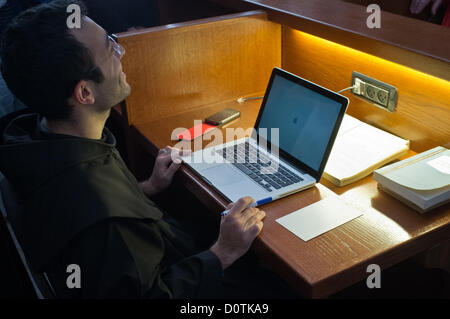 Jerusalem, Israel. 30th November 2012. A young Franciscan monk is busy studying in the Franciscan Terra Sancta compound library using an Apple Mac Book and with an iPhone on the desk to his left. Jerusalem, Israel. 30-Nov-2012.  Of the 20,000 Franciscan monks worldwide about 300 reside in Israel as well as some 1,000 nuns. Saint Francis Francesco of Assisi first arrived in the Holy Land in 1219 and they have been custodians of the holy sites ever since. Stock Photo