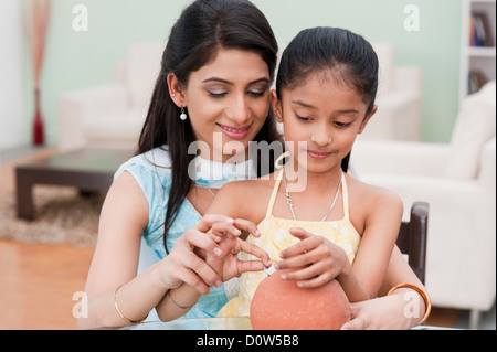 Woman and her daughter inserting a coin into a piggy bank Stock Photo