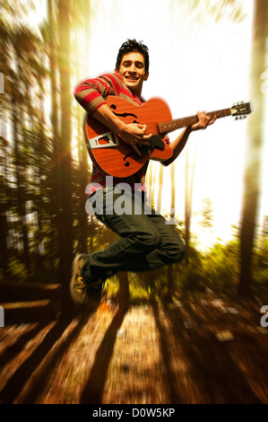 Man playing a guitar and jumping in a forest, Gurgaon, Haryana, India Stock Photo