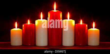 Still life photo of red and white church candles arranged in an arch burning with bright flames against a black background. Stock Photo