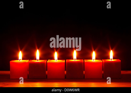 Still life photo of six square red candles burning bright against a black background. Stock Photo