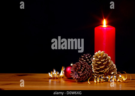 Still life photo of a Christmas candle burning bright with gold pine cones and ribbon plus a red bauble Stock Photo