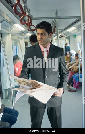 Businessman reading a newspaper in a subway train, New Delhi, India Stock Photo