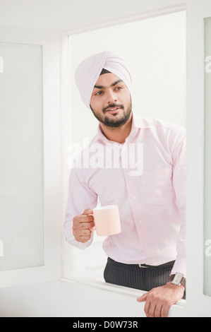 Businessman holding a coffee cup and looking out of a window Stock Photo