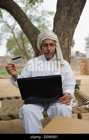 Farmer holding a credit card and using a laptop, Hasanpur, Haryana, India Stock Photo